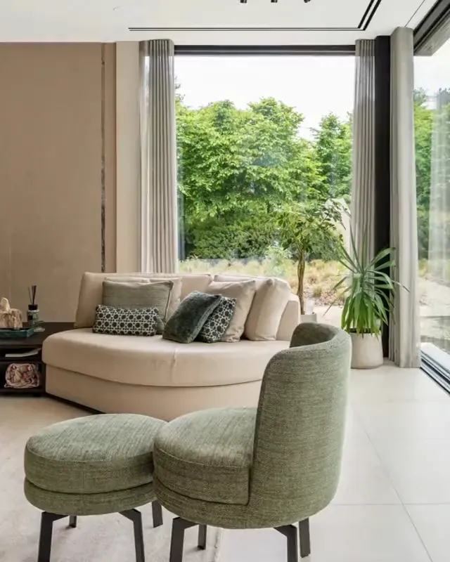 Standbild: Wohnbereich mit hellem Sofa, grünen Sesseln und grosser Fensterfront